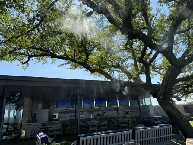 Misting fans producing cooling mist through an oak tree canopy at the rooftop bar